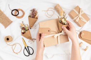 person's hands wrapping gifts with brown paper and adding fresh flowers