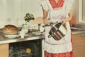 1950s Housewife loads the dishes in the dishwasher.