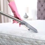woman wearing pink cleaning gloves steam cleaning a mattress