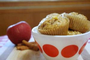 apple cinnamon muffins in white bowl with red dots with apple and cinnamon in background