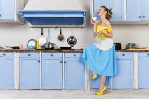 1950s housewife in blue and yellow dress with yellow heels, sipping tea in vintage kitchen