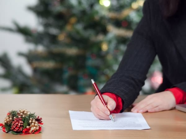 person writing a list in front of christmas tree