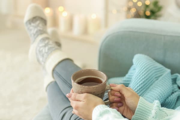 woman in cozy socks on sofa with cup of tea
