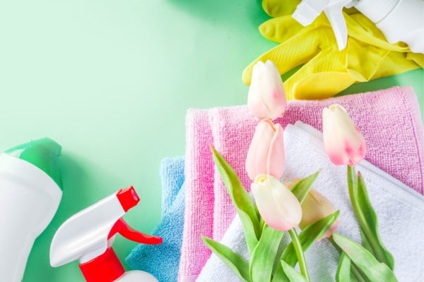 cleaning supplies, towels, and pink tulips on green background
