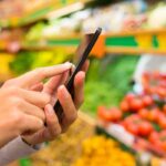woman holding phone while shopping for produce
