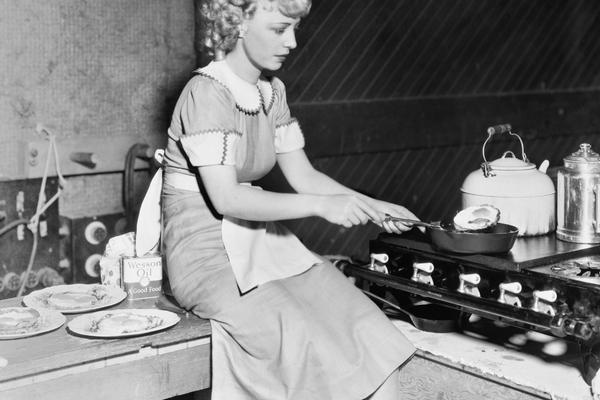 vintage housewife wearing a house dress while sitting on counter cooking