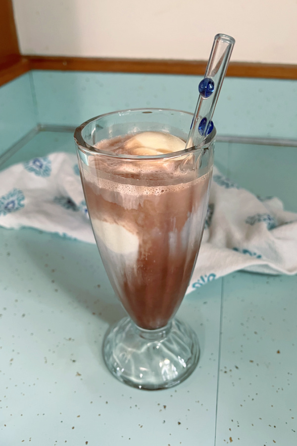 chocolate soda with vanilla ice cream in glass with glass straw with dish towel in background 